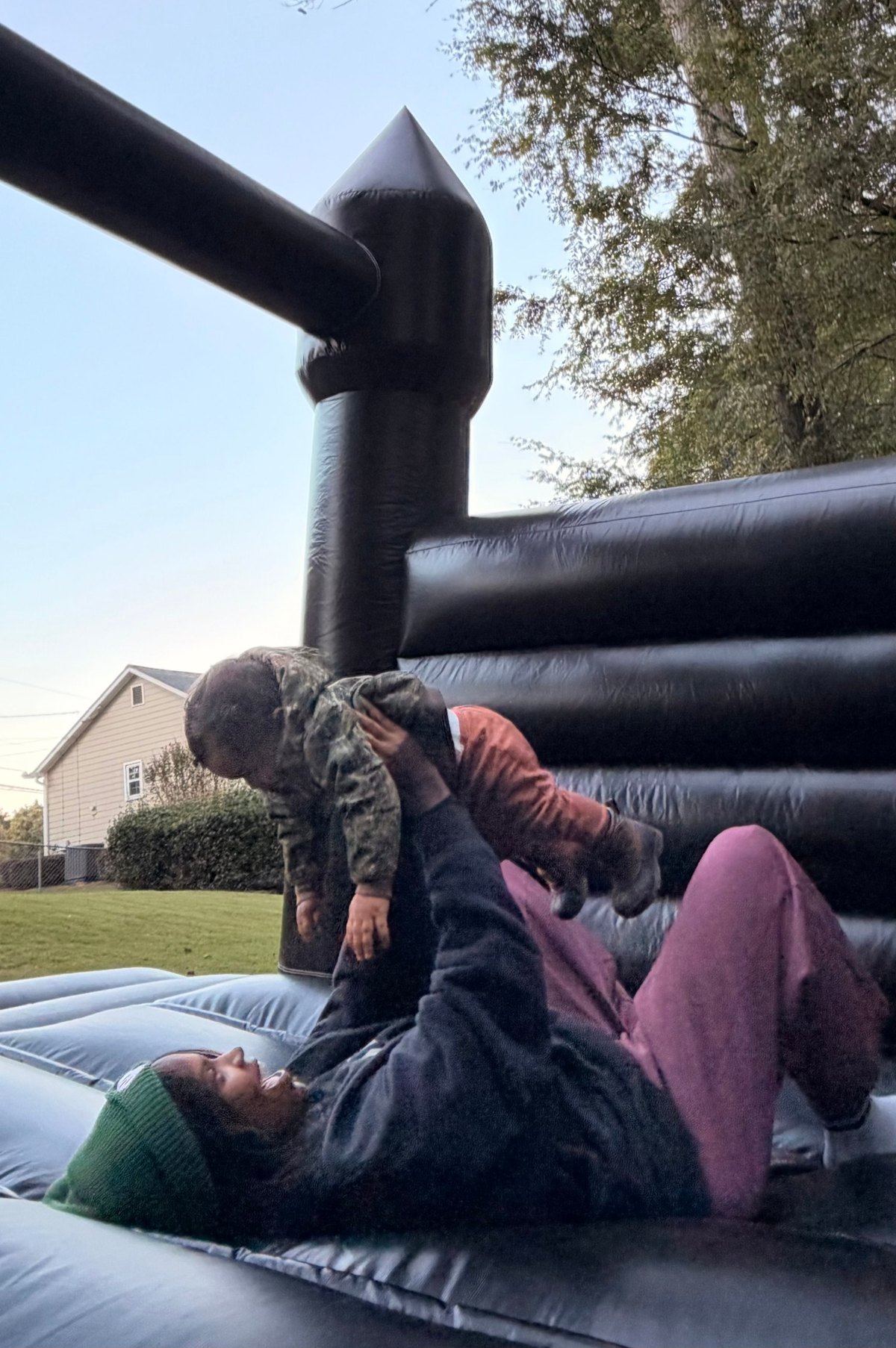 The founder lying on a black bounce house, lifting her baby son up overhead and smiling